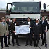 Personen halten einen Scheck vor einem LKW 